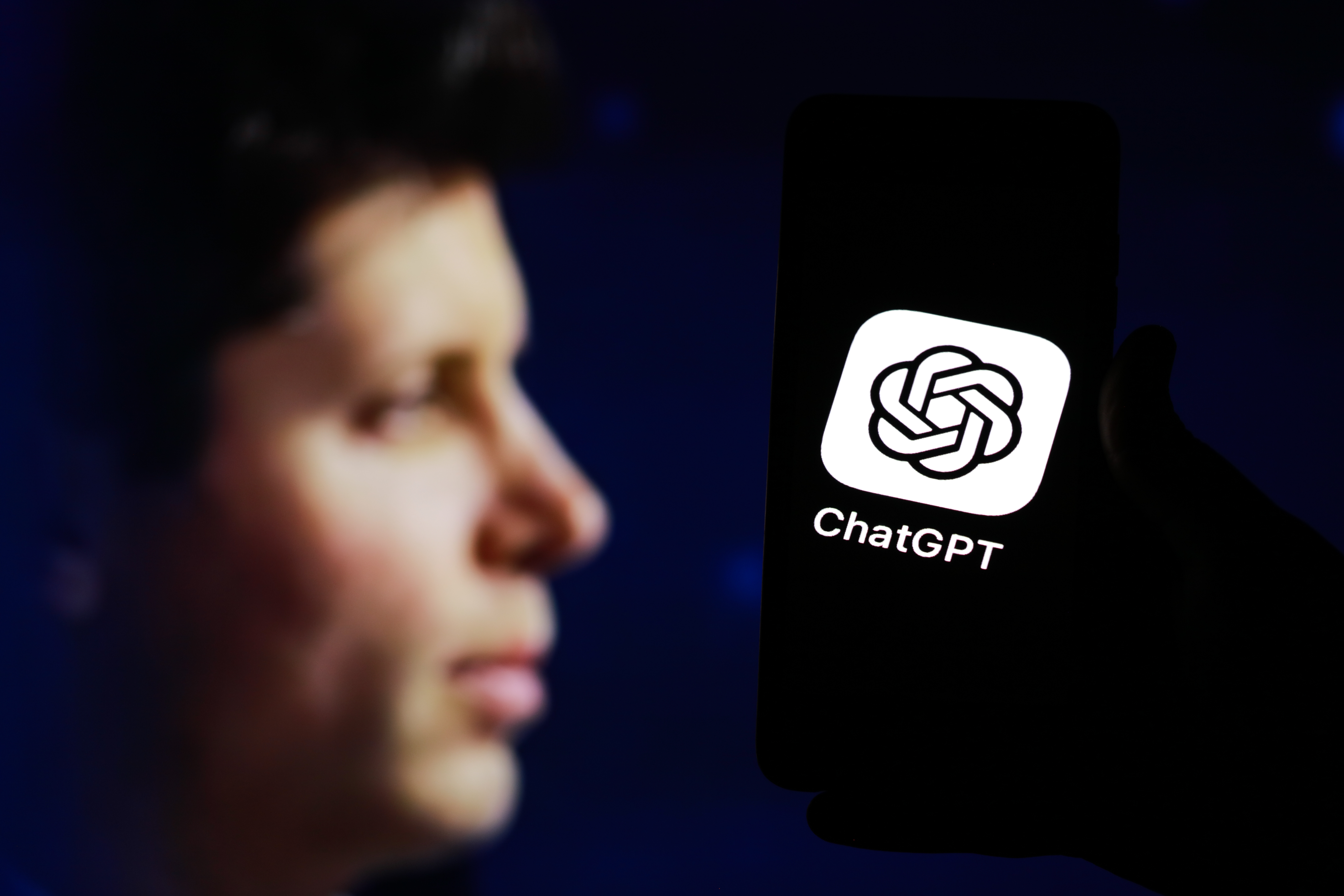 Person holding a smartphone displaying the ChatGPT app logo against a dark background.